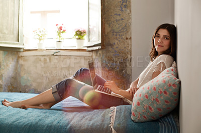 Buy stock photo Portrait of a smiling young woman lying on her bed using a laptop