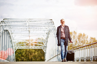 Buy stock photo Shot of a mature man pulling a suitcase while walking over a bridge in the city