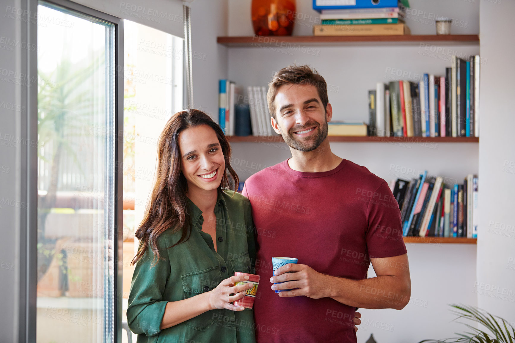 Buy stock photo Portrait of a smiling young couple standing together in their living room drinking coffee