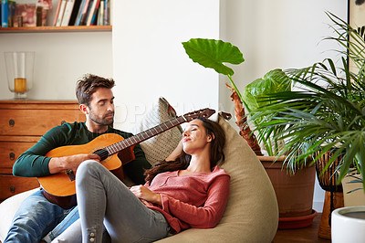 Buy stock photo Shot of a young man playing guitar for his girlfriend while relaxing in their living room