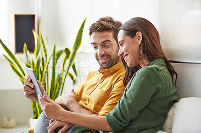 Buy stock photo Shot of a smiling young couple using a digital tablet together while relaxing in their living room