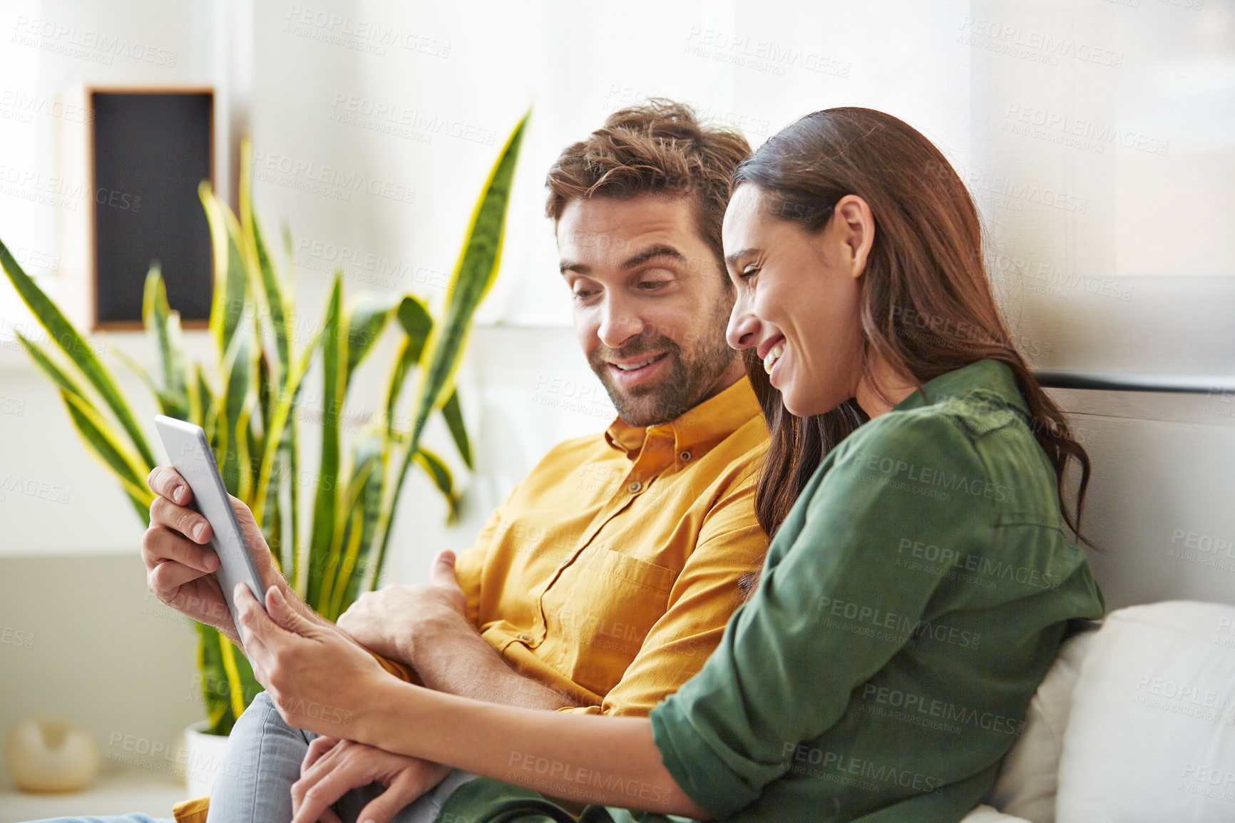 Buy stock photo Shot of a smiling young couple using a digital tablet together while relaxing in their living room