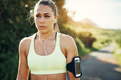 Buy stock photo Shot of a focused young woman listening to music on headphones before going for a run