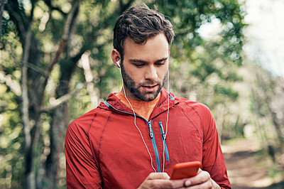Buy stock photo Shot of a young man listening to music on an mp3 player while out for a run in the forest