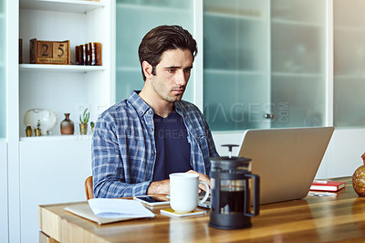 Buy stock photo Shot of a handsome young man working on his laptop at home