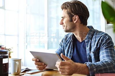 Buy stock photo Shot of a handsome young man working on his tablet at home
