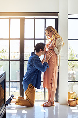 Buy stock photo Shot of a handsome young man kissing his pregnant wife's tummy at home
