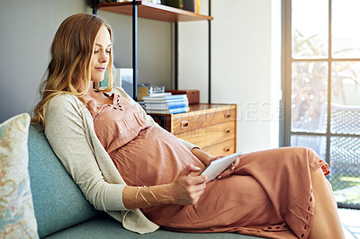 Buy stock photo Shot of a young pregnant woman using a tablet while sitting on the sofa at home