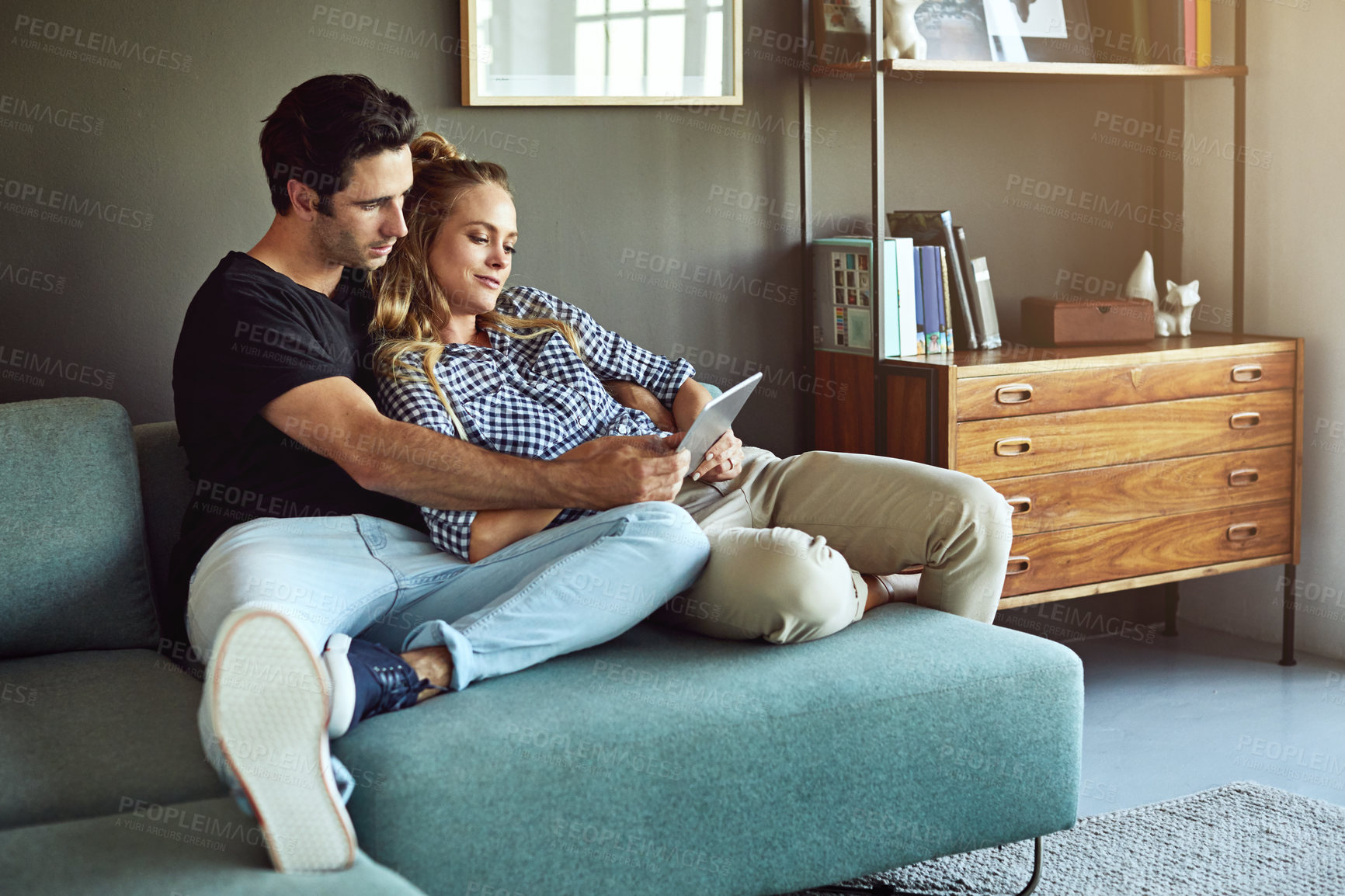 Buy stock photo Shot of an affectionate young couple using a tablet while sitting on a sofa at home