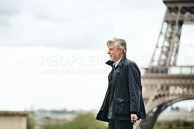 Buy stock photo Shot of a handsome mature man walking with his suitcase in front of the Eiffel Tower