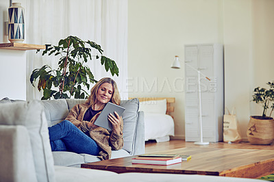 Buy stock photo Shot of a mature woman using her tablet while relaxing on the sofa at home
