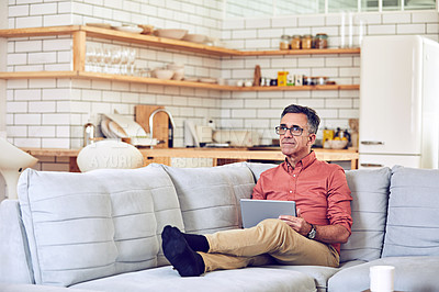 Buy stock photo Shot of a handsome and mature man using a tablet while relaxing on the sofa