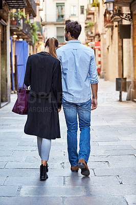 Buy stock photo Rearview shot of an affectionate young couple walking arm in arm together in the city