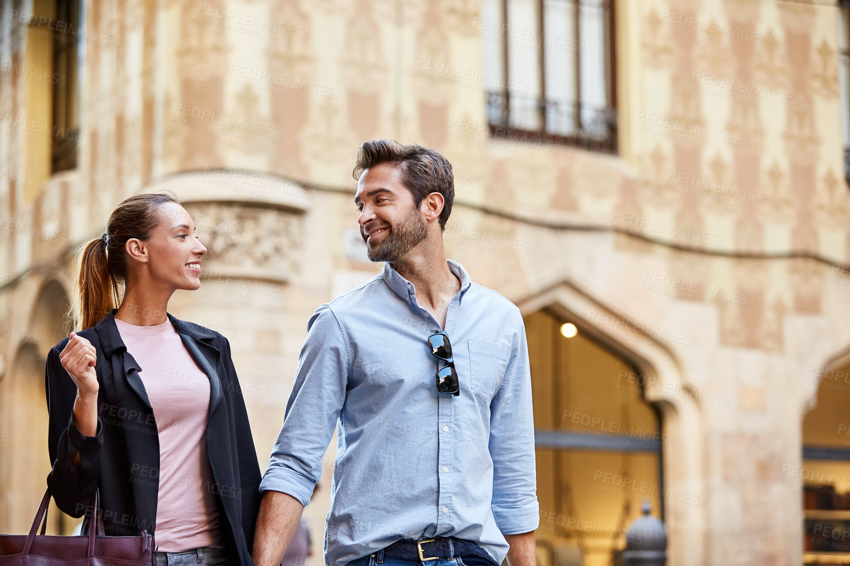 Buy stock photo Shot of an affectionate young couple walking hand in hand together in the city