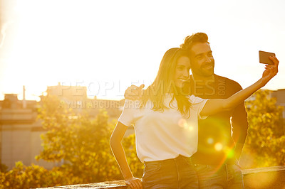 Buy stock photo Shot of an affectionate couple taking a selfie while sitting on a balcony overlooking the city at sunset