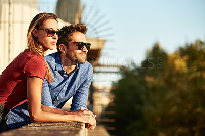 Buy stock photo Shot of a smiling young couple talking together while leaning on a balcony in the city looking at the view