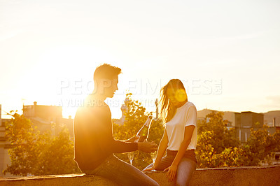 Buy stock photo Shot of a smiling couple drinking champagne while sitting on their rooftop at sunset