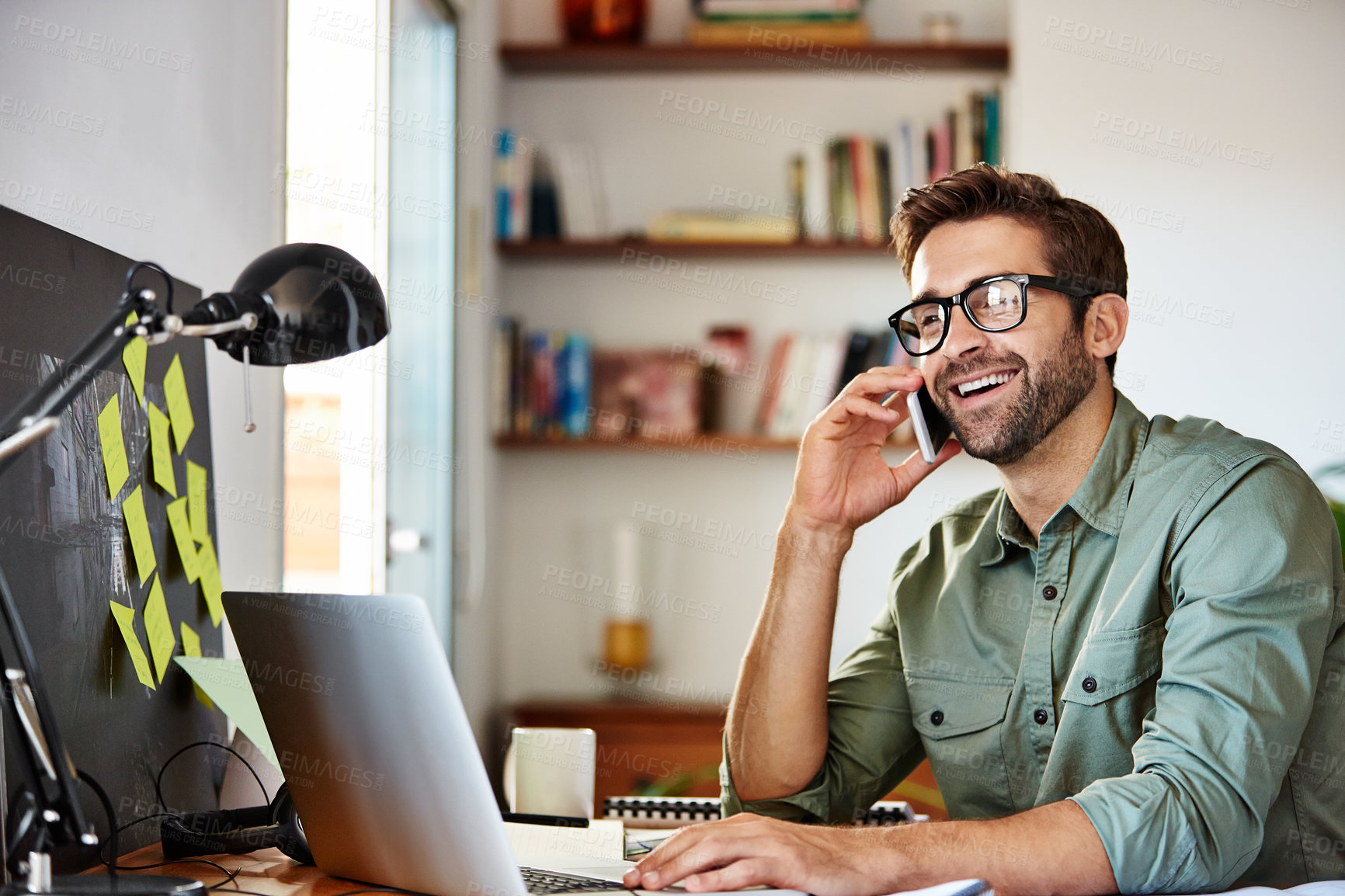 Buy stock photo Shot of a young man using he cellphone while sitting at a table and working from home