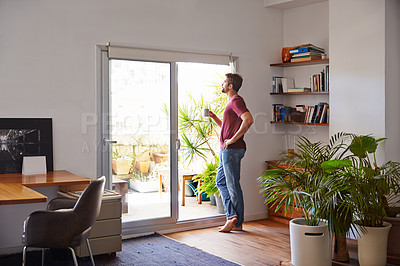 Buy stock photo Shot of a handsome young man standing in his living room drinking coffee