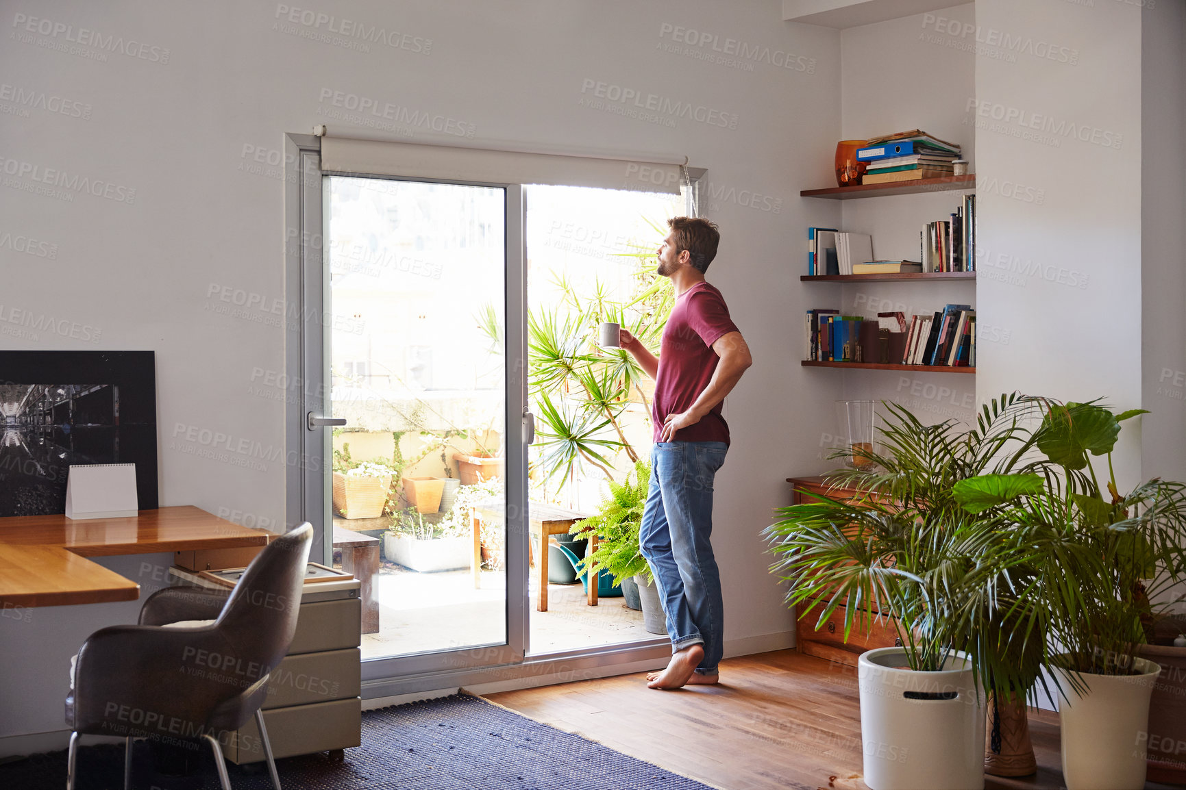 Buy stock photo Shot of a handsome young man standing in his living room drinking coffee