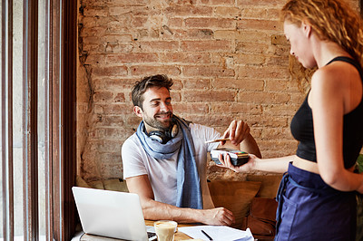 Buy stock photo Shot of a handsome young man using NFC technology to pay his waitress in a cafe