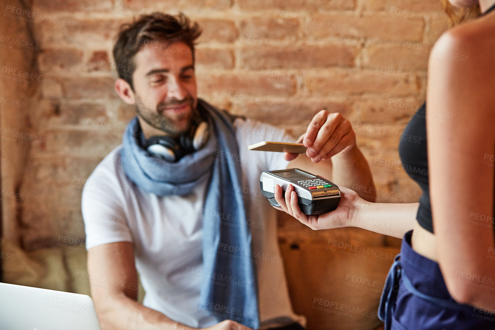 Buy stock photo Shot of a handsome young man using NFC technology to pay his waitress in a cafe
