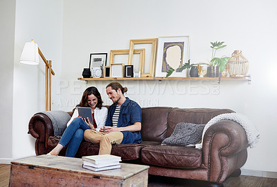 Buy stock photo Shot of an affectionate young couple using a tablet while sitting on their sofa at home