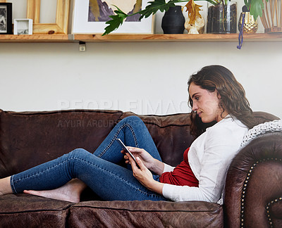 Buy stock photo Shot of an attractive young woman using a tablet while relaxing on a sofa at home