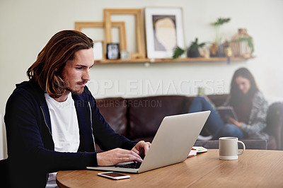 Buy stock photo Shot of a handsome young man working at home with his wife in the background