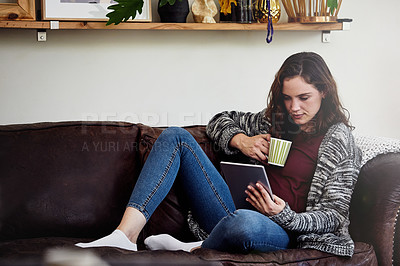Buy stock photo Shot of an attractive young woman using a tablet while relaxing on a sofa at home