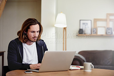 Buy stock photo Shot of a handsome young man working on his laptop at home