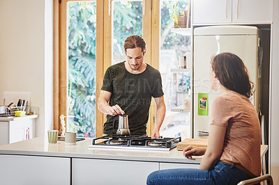 Buy stock photo Shot of a handsome young man preparing coffee in the kitchen while talking to his wife