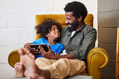Buy stock photo Shot of a cheerful young father and son relaxing on a chair while browsing on a digital tablet at home