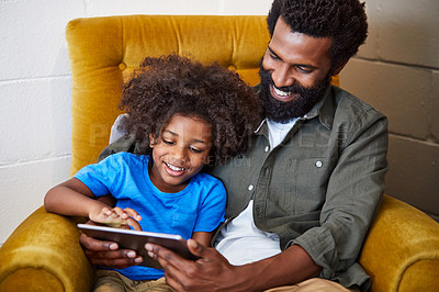 Buy stock photo Shot of a cheerful young father and son relaxing on a chair while browsing on a digital tablet at home