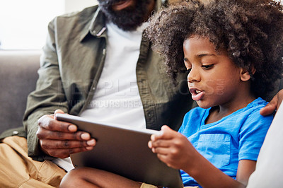 Buy stock photo Shot of a cheerful young father and son relaxing on a chair while browsing on a digital tablet at home