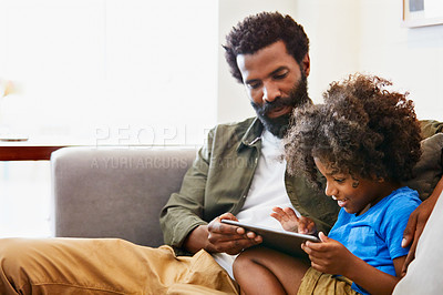Buy stock photo Shot of a cheerful young father and son relaxing on a chair while browsing on a digital tablet at home