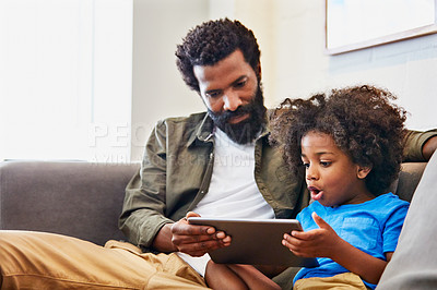 Buy stock photo Shot of a cheerful young father and son relaxing on a chair while browsing on a digital tablet at home