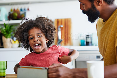 Buy stock photo Portrait of a cheerful young father and son browsing on a digital tablet while having a cup of coffee in the kitchen at home