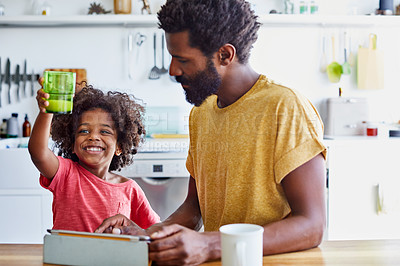 Buy stock photo Shot of a cheerful young father and son browsing on a digital tablet while having a cup of coffee in the kitchen at home