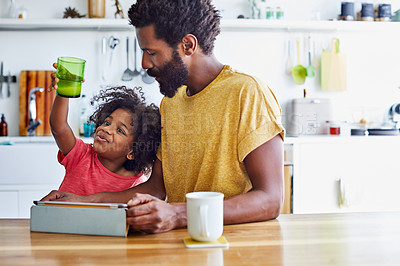 Buy stock photo Shot of a cheerful young father and son browsing on a digital tablet while having a cup of coffee in the kitchen at home