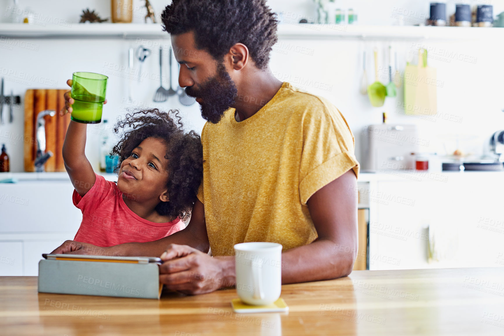 Buy stock photo Shot of a cheerful young father and son browsing on a digital tablet while having a cup of coffee in the kitchen at home