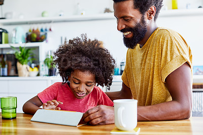 Buy stock photo Shot of a cheerful young father and son browsing on a digital tablet while having a cup of coffee in the kitchen at home