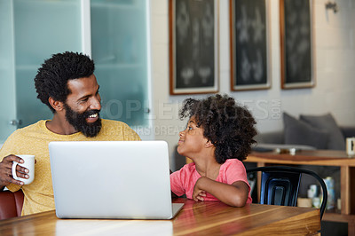 Buy stock photo Shot of a cheerful young father and son browsing on a laptop while having a cup of coffee in the kitchen at home