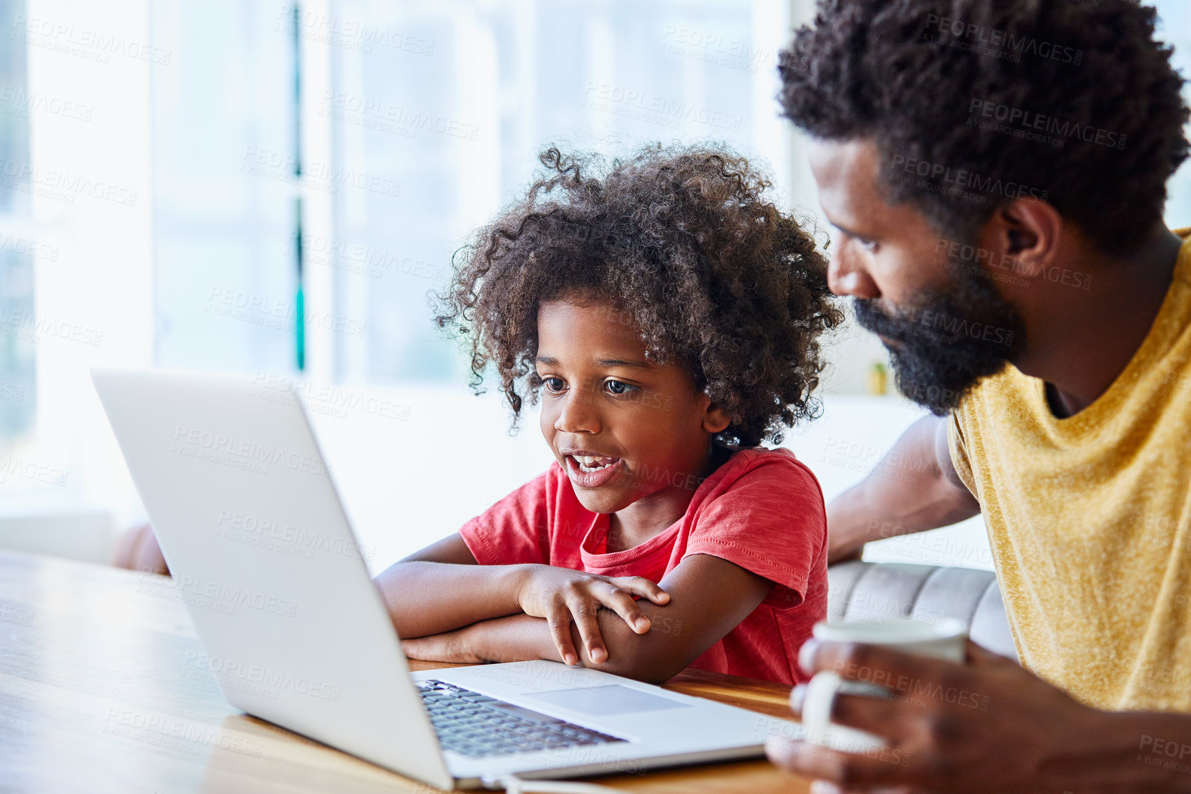 Buy stock photo Shot of a cheerful young father and son browsing on a digital tablet together while being seated at a table in their home