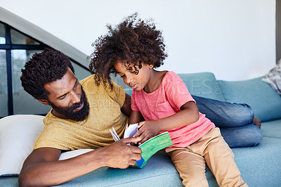 Buy stock photo Shot of a cheerful young father and son reading a storybook while being seated on a couch at home