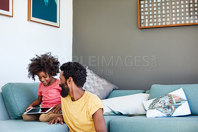Buy stock photo Shot of a cheerful young father and his son browsing on a digital tablet while being seated on a couch at home