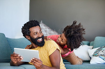Buy stock photo Shot of a cheerful young father and his son browsing on a digital tablet while being seated on a couch at home