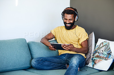 Buy stock photo Shot of a focused young man listening to music through headphones while being seated on a couch at home