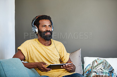 Buy stock photo Shot of a focused young man listening to music through headphones while being seated on a couch at home