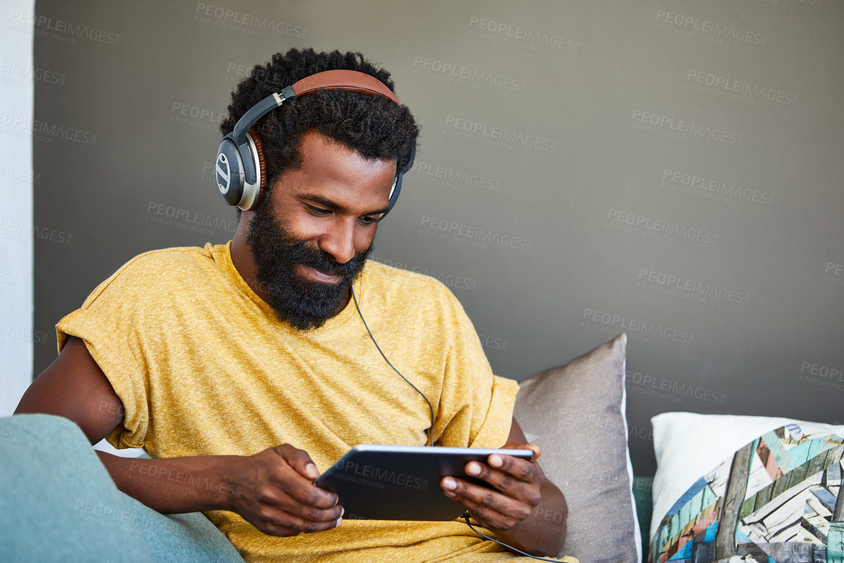 Buy stock photo Shot of a focused young man listening to music through headphones while being seated on a couch at home